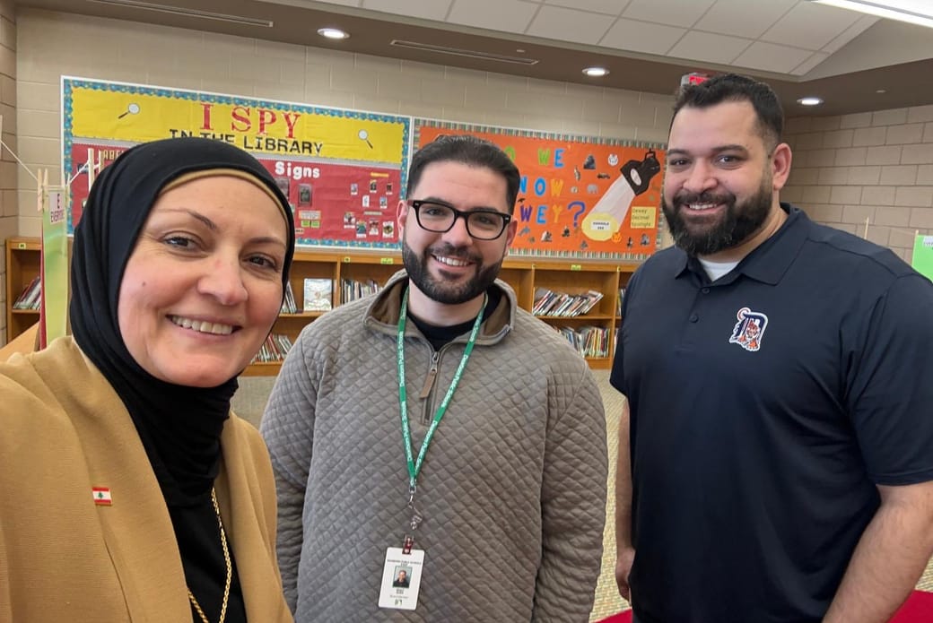 Nasri Sobh with two colleagues in a Dearborn elementary school library, wearing a Dearborn Public Schools staff badge.