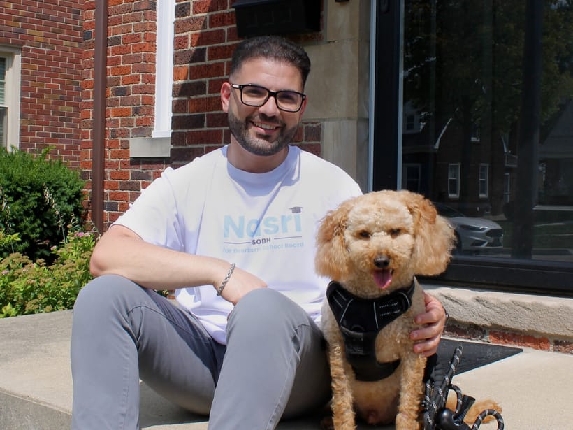 Nasri Sobh on the front steps of a Dearborn house with his dog, wearing a campaign shirt.